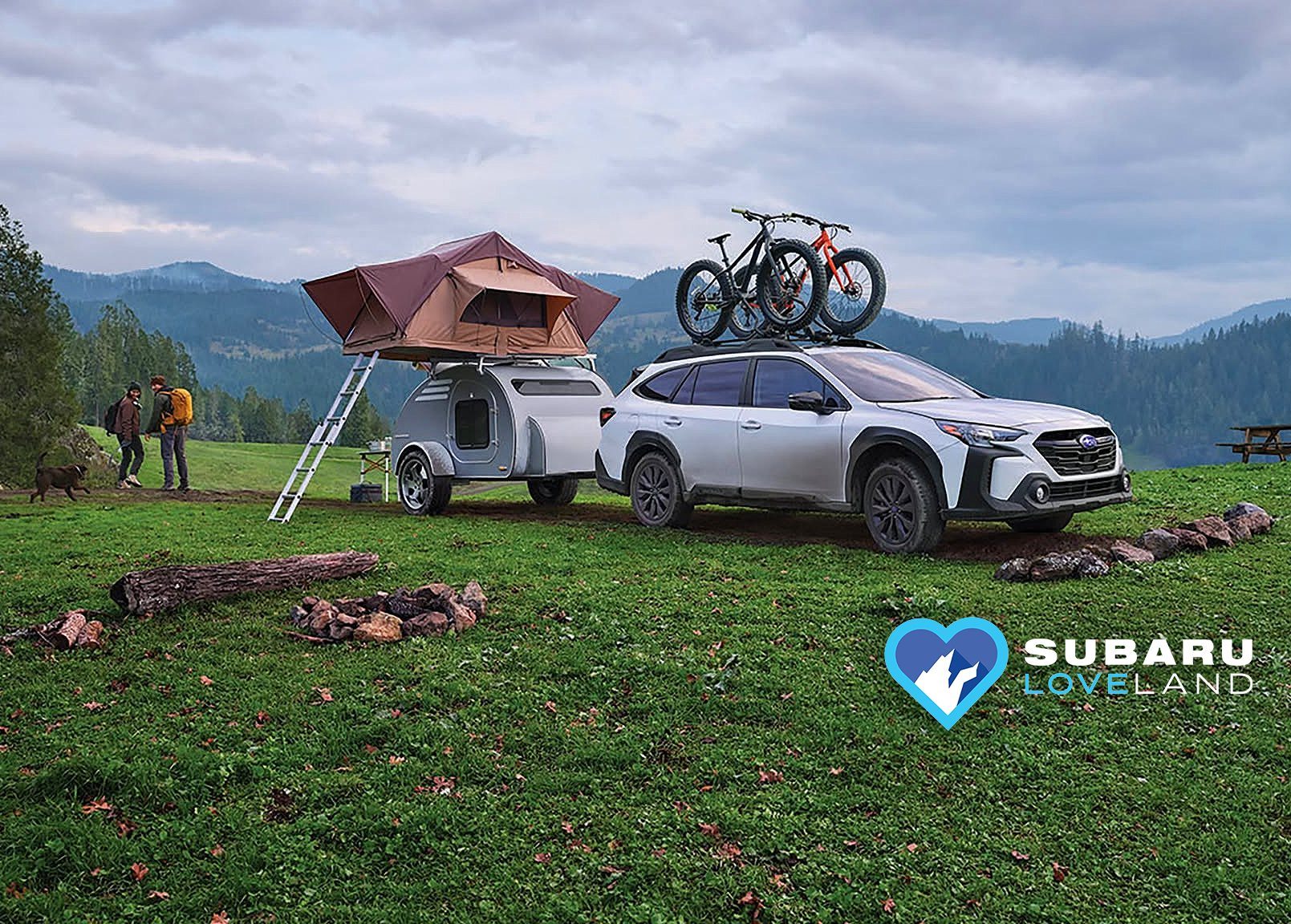 A Subaru with a roof tent and bikes parked in a mountain meadow with the Subaru Loveland heart logo